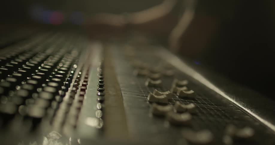 A man adjusts sliders and dials on a soundboard in a music studio