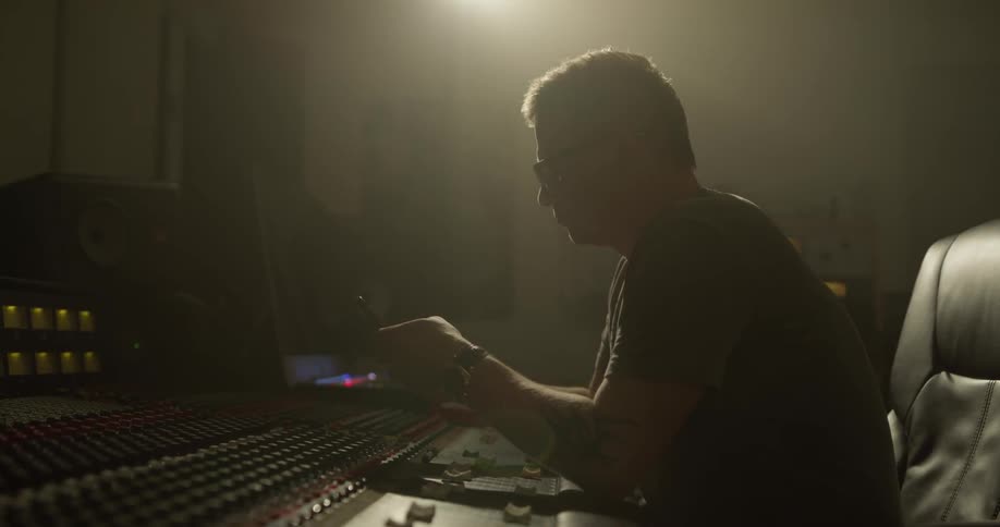 Man texts on a smartphone in front of a large control mixer