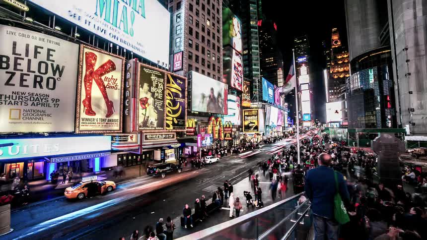 Colorful signs flicker in a busy city center with streams of pedestrians and cars going by