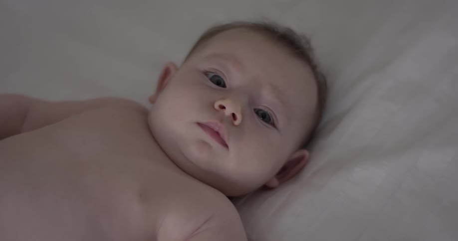A baby lays on a white sheet as it looks up