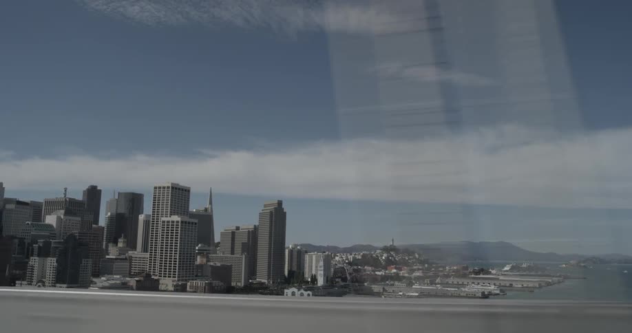 Car passes by fast driving down the road of a bridge that overlooks the city skyline in a bright sunny day