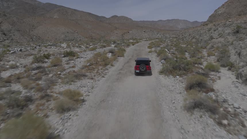 A jeep drives along a dusty path at midday