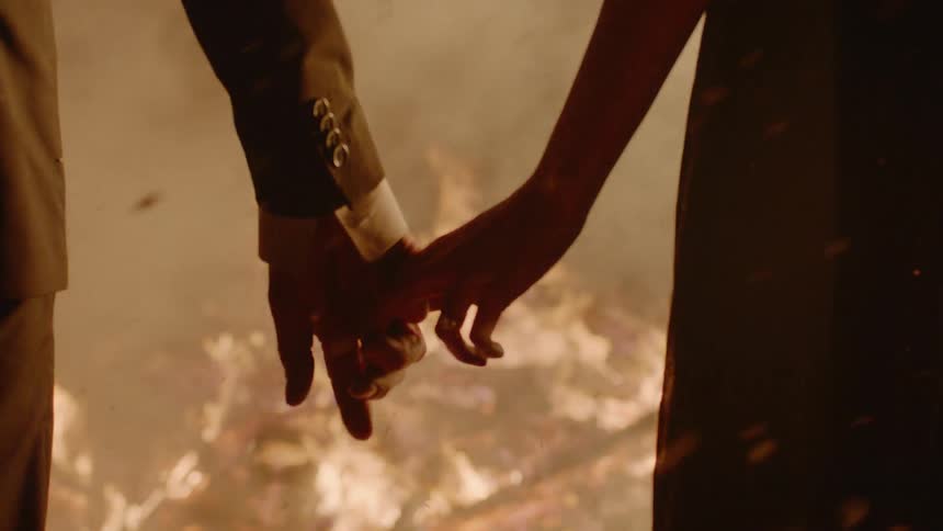 Two people are holding hands by a fire