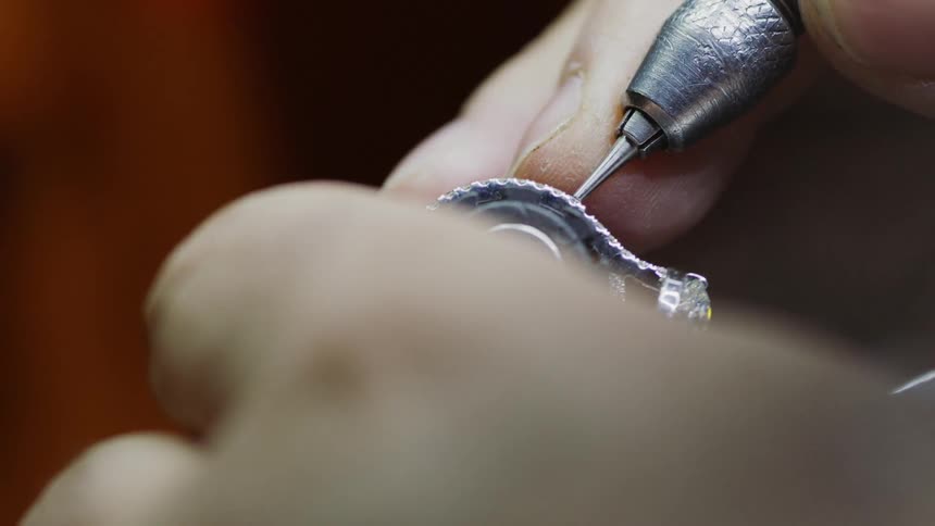 Soldering a metallic object perhaps an electronic device or a jewelry of sorts with white human hands indoors