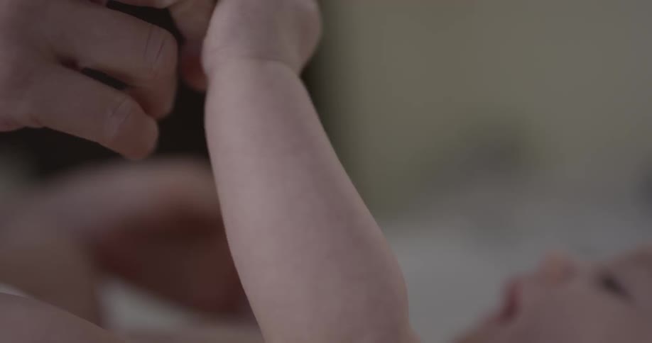 A baby holds its mothers hands while lying down
