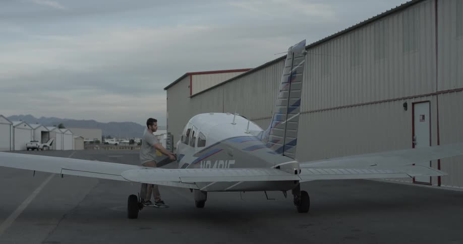 An airplane is inspected by a man with short hair and a beard on a nice cloudy but sunny day