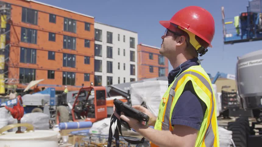 A construction worker looks at a tablet, and then up in the air