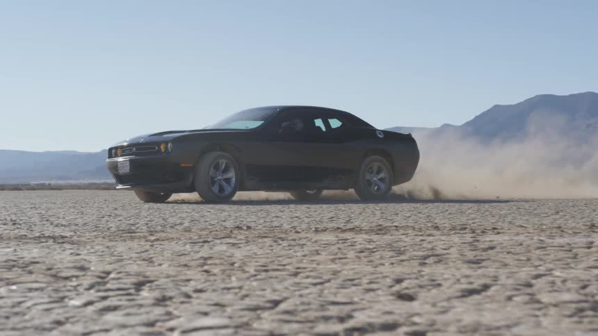Black car speeds in the desert leaving behind a cloud of smoke