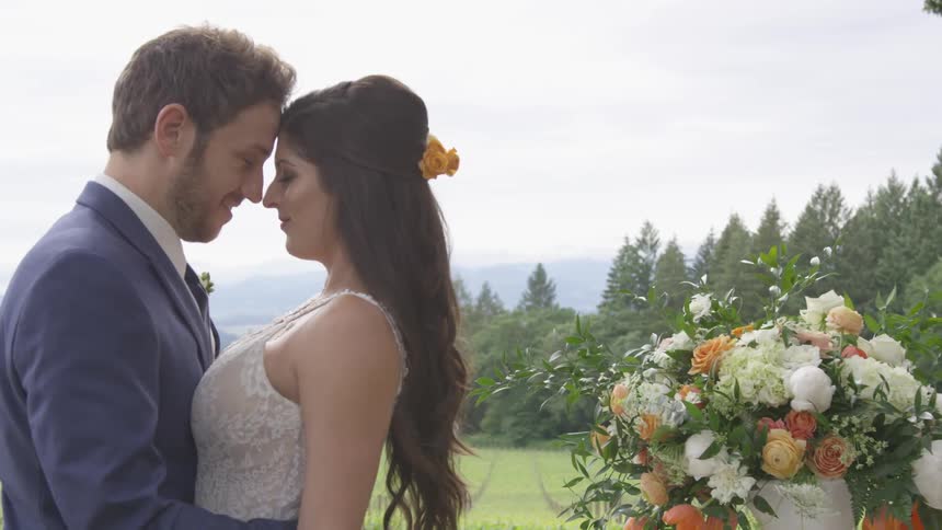A man and a woman stand with their foreheads touching next to a bouquet of flowers