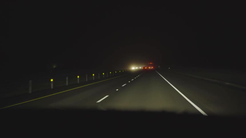 A car is driving on a road at night