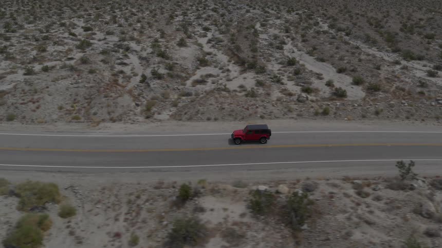 A jeep drives through the desert road with some vegetation around on a very bright sunny day