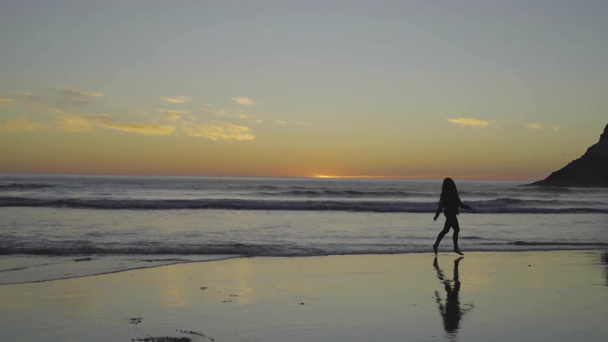 A woman is walking by a beach at sunset