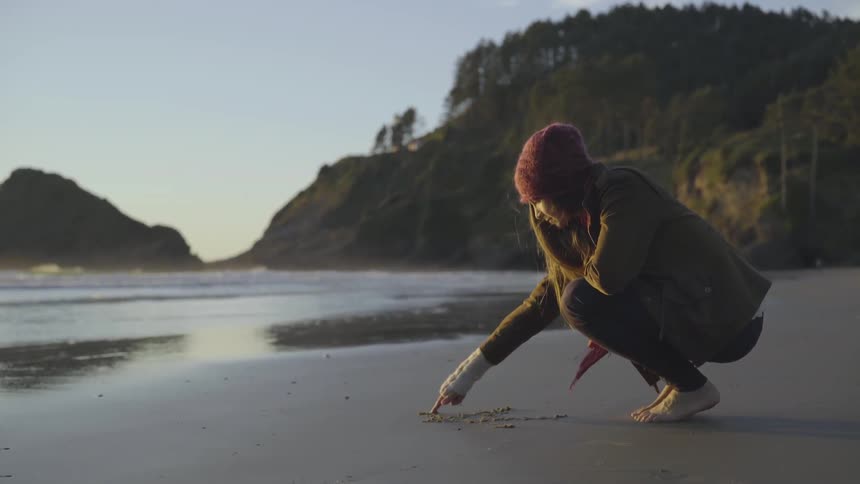 A woman draws in the sand with her fingertip