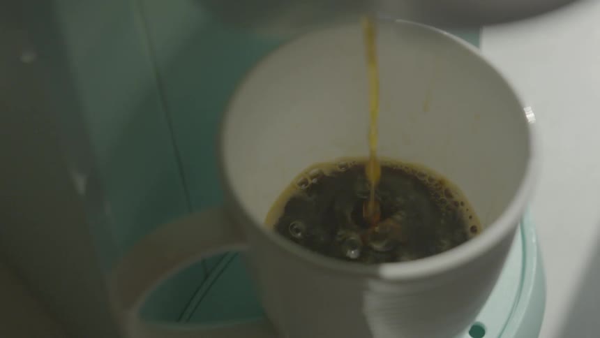 Coffee drips from a coffee maker into a white mug