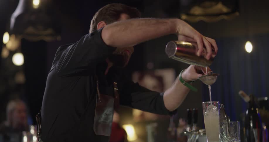 Male bartender pouring a drink through a strainer into a glass of ice