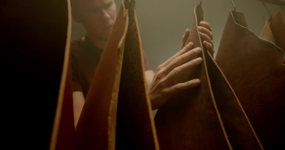 A man walks over and inspects pieces of leather that are hanging