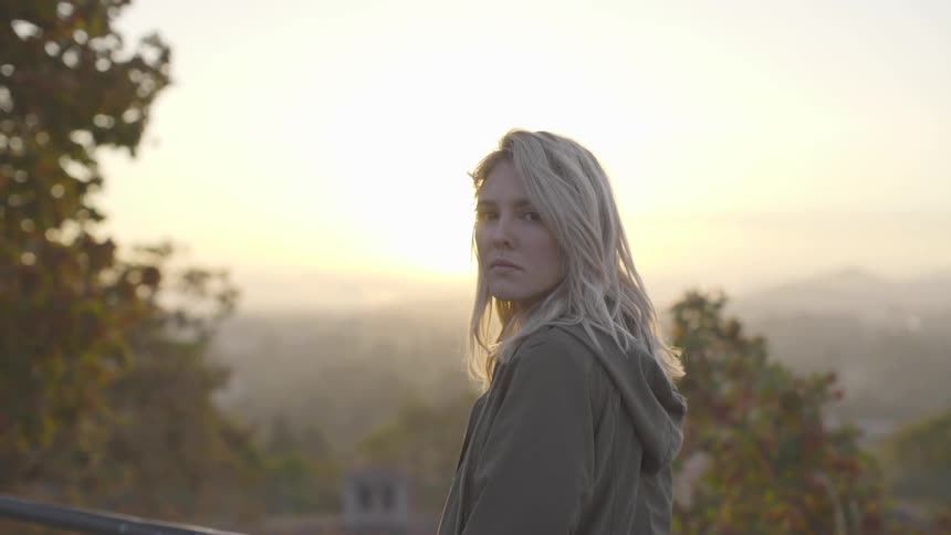 A woman stares to her left while the sun sets behind her