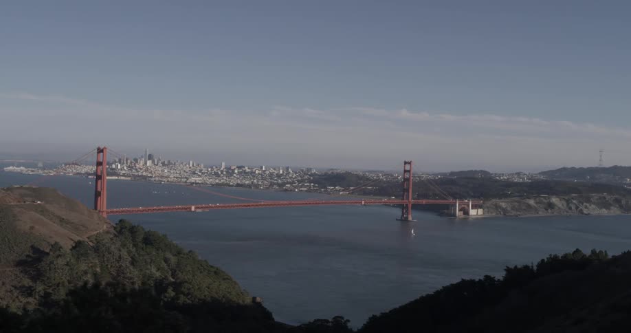 Long red bridge connects two points over wide blue water near city