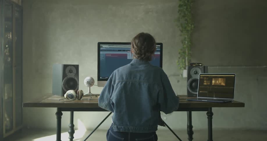 A woman looks at a laptop and a large computer screen