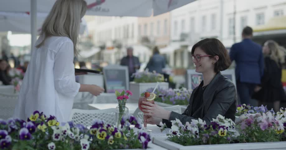 A waitress serves a cocktail to a woman sitting at an outdoor table