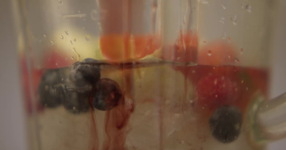 Syrup drips down the side of a glass with berries and fruit and ice