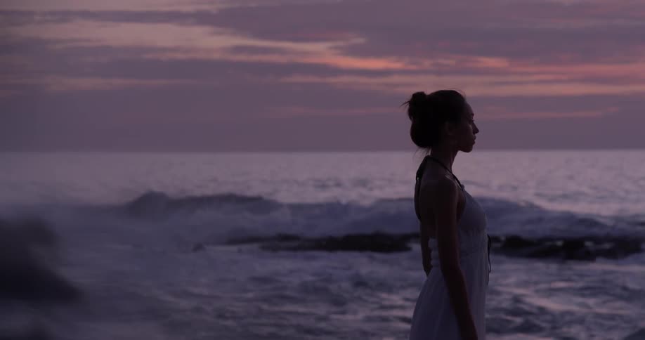 Woman stands on the beach at sunset with waves crashing behind her