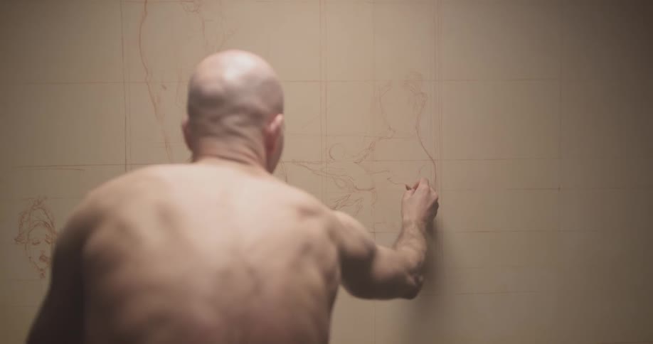 Shirtless man sketches on the wall