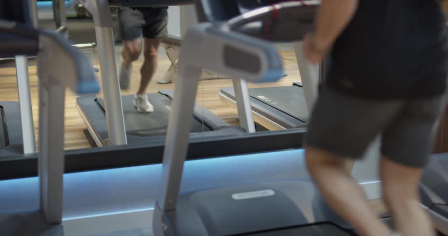Man runs on a treadmill at a gym in front of a mirror