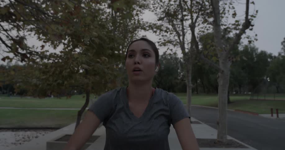 Woman walks along sidewalk near pond stretching