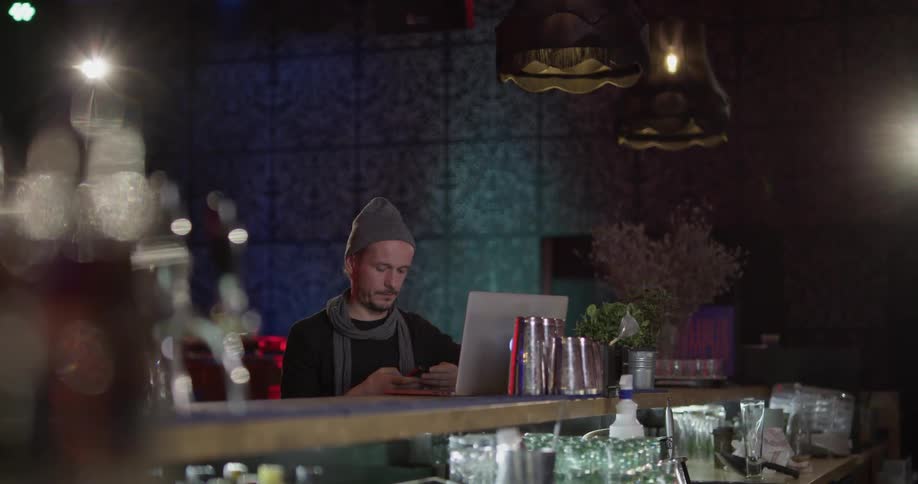 Man sits at bar with laptop talking on phone