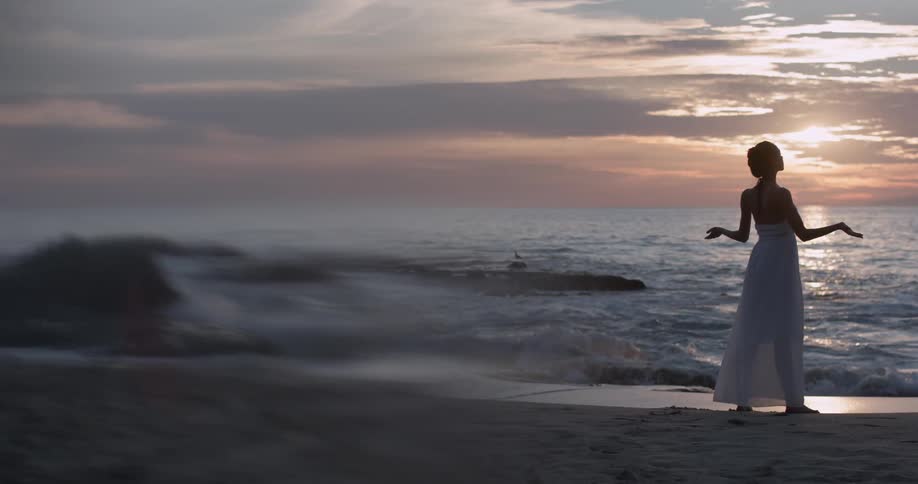 Woman spreads her hands in enjoyment as she watches the sunset over ocean