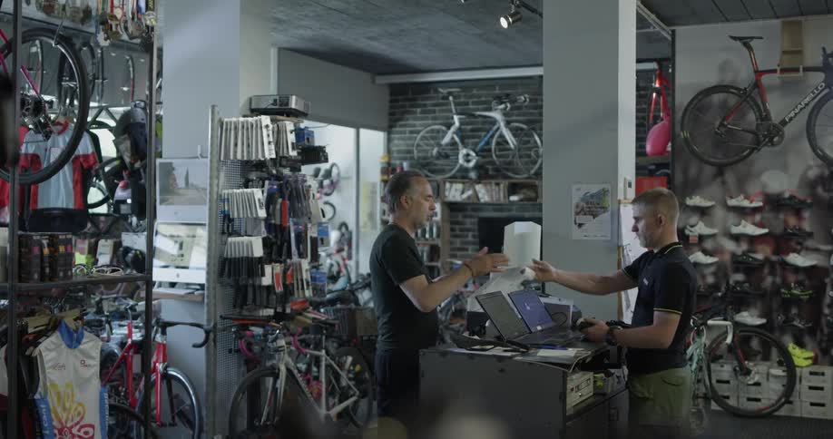 Two men in a bike shop are standing near the computers