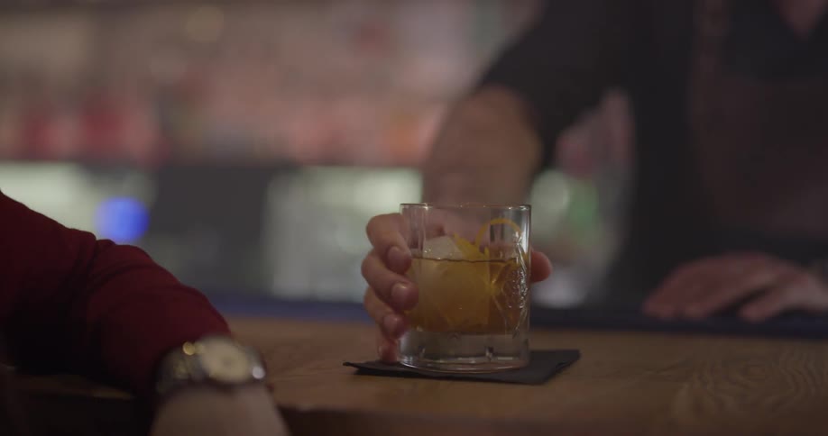 A bartender puts a drink down on a napkin in front of a customer who picks it up