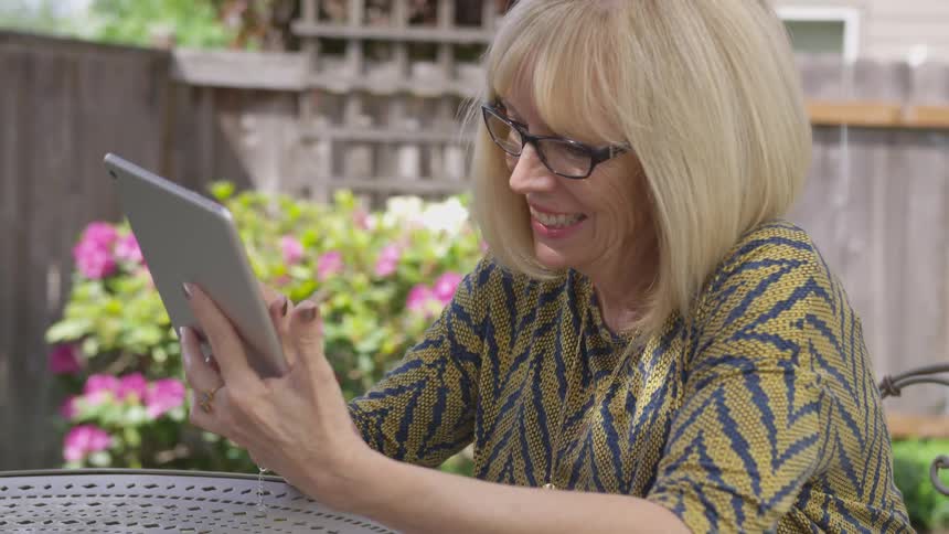 A woman smiles while scrolling on a tablet on a patio