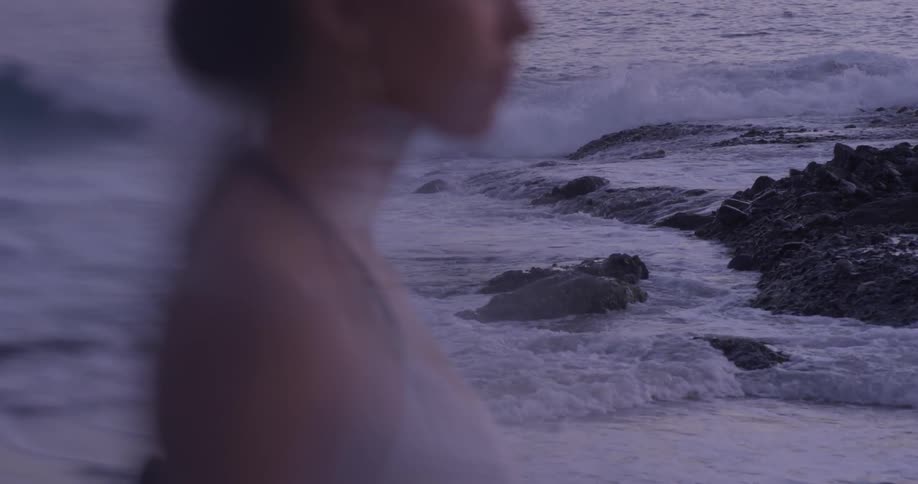 Woman stands on beach and waves crash onto beach behind her