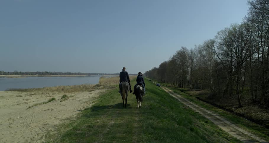 Two people riding horses along a water edge