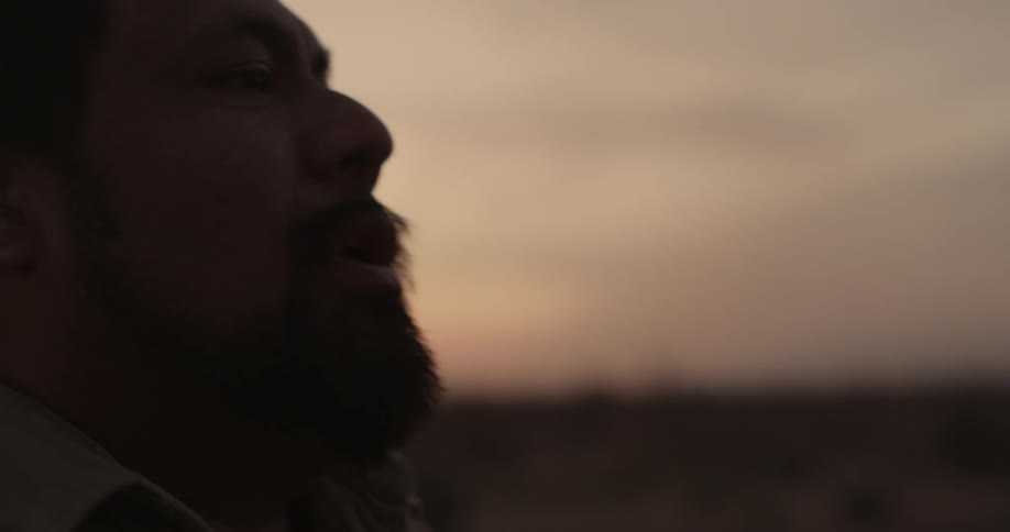 A man takes a drag from a cigarette as he stands under a cloudy sky at dusk