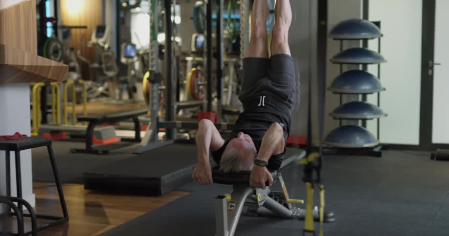 An elderly man does leg lifts on a workout bench