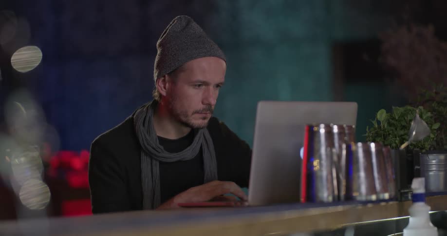 Man in hat works on laptop at bar
