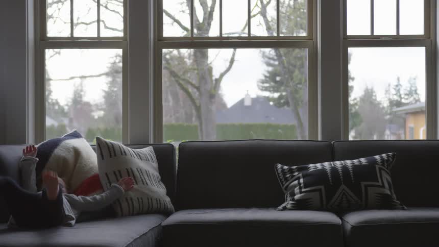 A child walks across a couch and flops herself on it inside at day