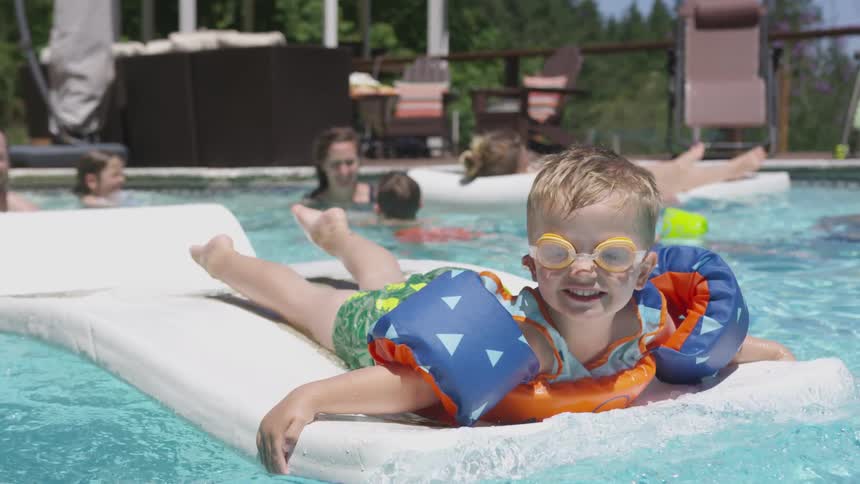 Young boy in goggles and puddle jumper floats on mat in swimming pool