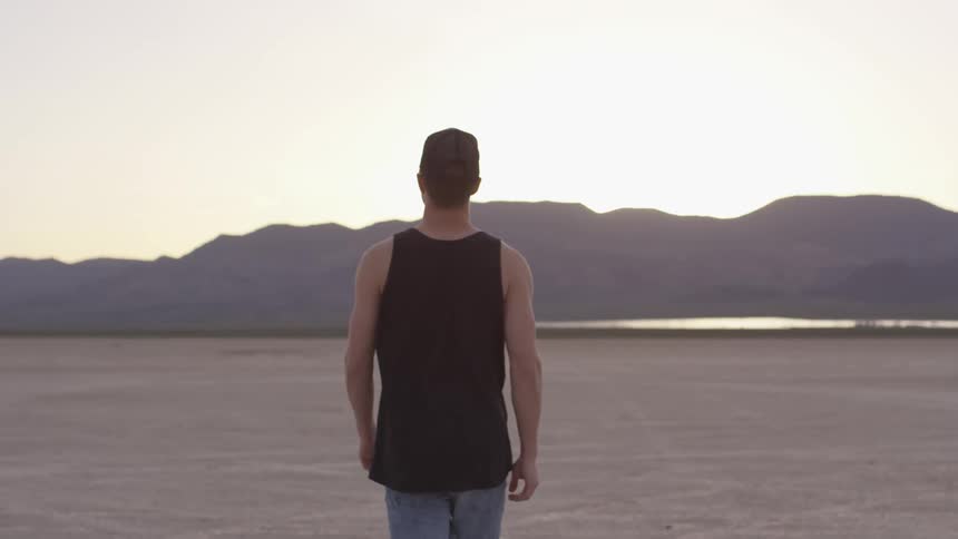 Man walks across desert towards mountains at sunset