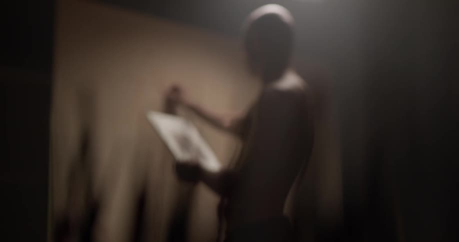 Man looks at a reference and sketches on a large white wall
