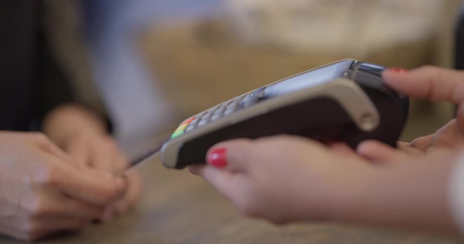 A woman holds a debit card machine toward another woman that taps her card on the machine