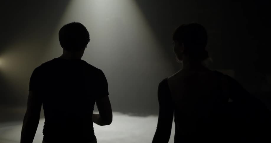 Two people walking toward a spotlight on stage