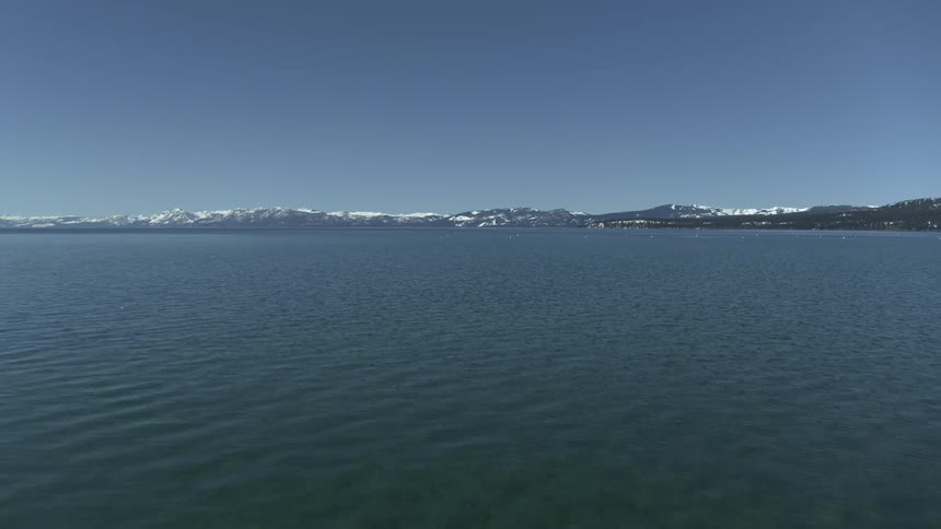 Water ripples under blue sky with snow covered mountains in the distance