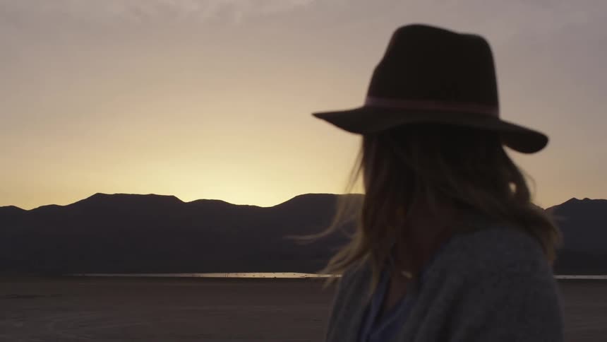 A woman standing in a dry lakebed at dusk