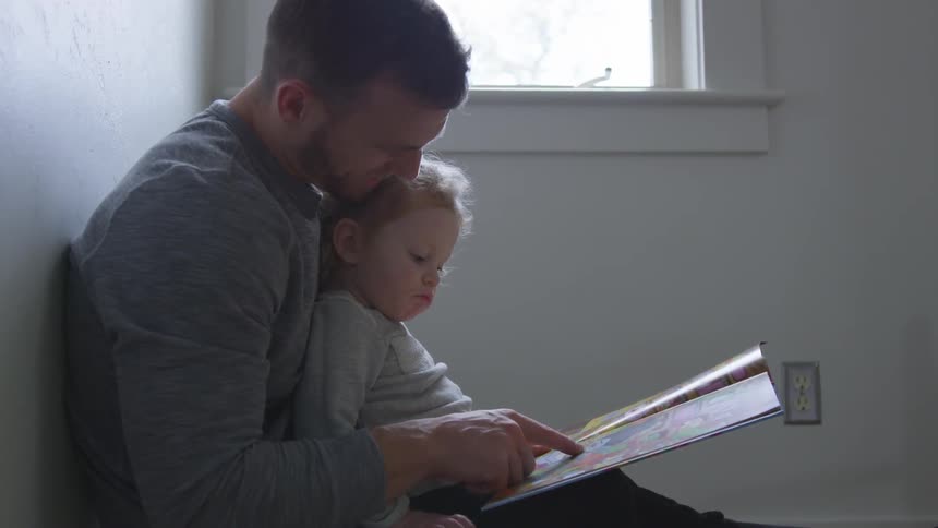 Man  holds girl in room and shows her book
