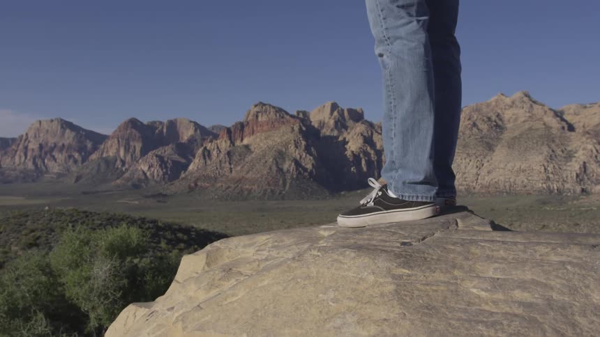 Man stands on rock overlooking valley with more mountains in background during the day