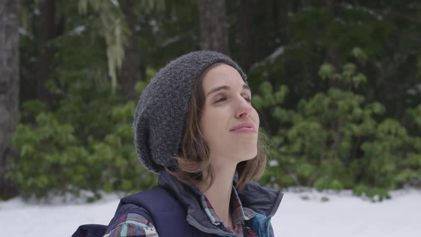 A woman wearing a backpack looking around at a forest
